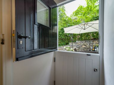 A half open stable door leading to a garden with a white patio umbrella and stone wall at Fellside Lodge in Bowness-On-Windermere
