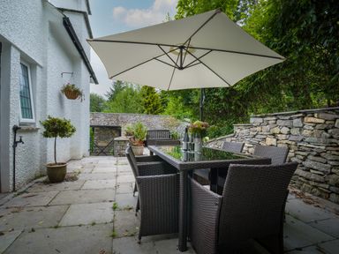 An outdoor patio with a table and six chairs under a large umbrella at Fellside Lodge in Bowness-On-Windermere