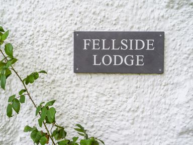 A sign reading Fellside Lodge on a textured white wall with green leaves on the side at Fellside Lodge in Bowness-On-Windermere