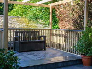 An outdoor deck with wooden railing a dark bench and potted plants at Fellside Lodge in Bowness-On-Windermere