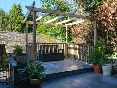 An outdoor wooden pergola with a bench and potted plants on a stone patio at Fellside Lodge in Bowness-On-Windermere