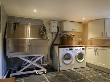 A utility room with a stainless steel washing station two white washing machines wooden countertop cabinets and a basket Fellside Lodge Bowness-On-Windermere