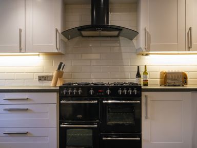 A kitchen with white cabinets a black stove a knife block two bottles and a toaster at Fellside Lodge in Bowness-On-Windermere