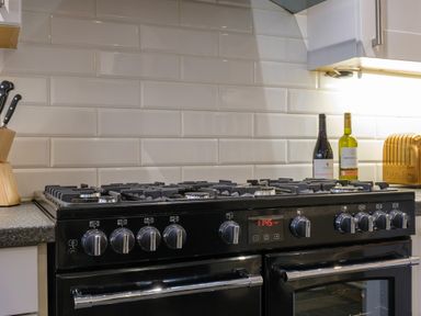 A kitchen stove with multiple burners and control knobs next to a knife block bottles of wine and a toaster at Fellside Lodge in Bowness-On-Windermere