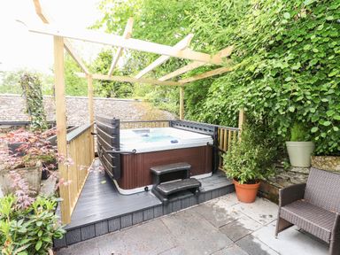 An outdoor patio area with a hot tub wooden pergola potted plants and a wicker chair at Fellside Lodge in Bowness-On-Windermere