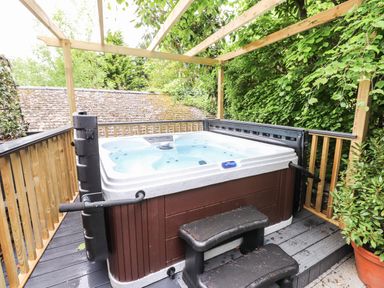 An outdoor hot tub on a wooden deck with steps and a wooden pergola surrounded by greenery at Fellside Lodge in Bowness-On-Windermere