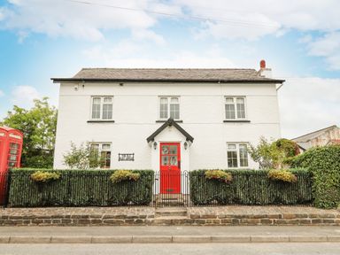 A white two-story house with a red door and black fence surrounded by greenery at The Old Post Office in Llandrindod Wells
