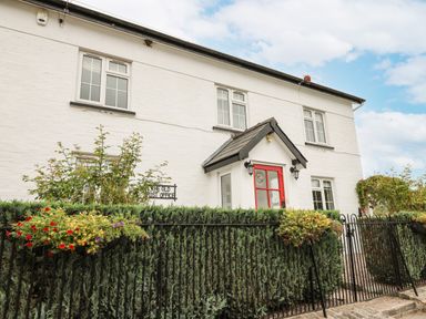 A white two-story house with a red door and iron fence with flower baskets at The Old Post Office in Llandrindod Wells
