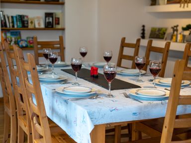 A dining table set with plates wine glasses and cutlery in a room with wooden chairs and shelves at The Old Post Office in Llandrindod Wells