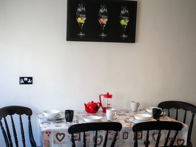 A dining table set with plates cups teapot and French press surrounded by black chairs at The Old Post Office in Llandrindod Wells