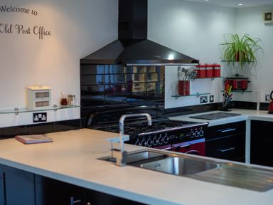 A kitchen with a stove black tiled backsplash and a sink with a faucet at The Old Post Office in Llandrindod Wells