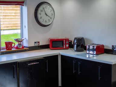A kitchen corner with a wall clock red microwave black air fryer red toaster red mug and scale at The Old Post Office in Llandrindod Wells