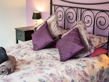 A bedroom with a bed with floral bedding purple and gray pillows a bedside table and a lamp at The Old Post Office in Llandrindod Wells