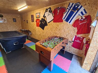 A game room with a foosball table and pool table with sports jerseys on the walls at The Old Post Office in Llandrindod Wells