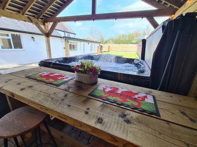 A wooden outdoor table with two red dragon placemats and a flower pot under a wooden pavilion next to a bubbling hot tub at The Old Post Office in Llandrindod Wells