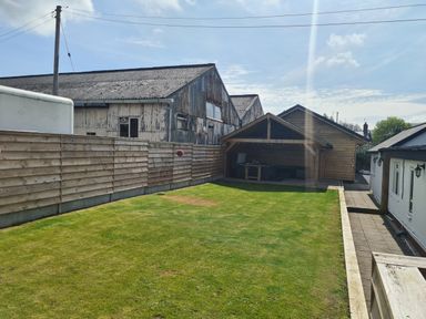 A backyard with a grass lawn wooden fence and a wooden gazebo next to a white building at The Old Post Office in Llandrindod Wells