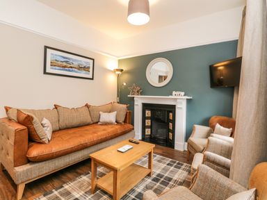 A living room with a sofa armchairs wooden coffee table fireplace and a wall-mounted TV at Netherbeck in Ambleside