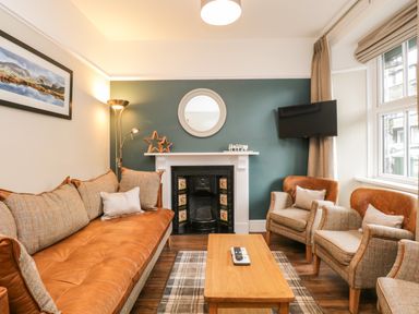A living room with a brown sofa two armchairs a wooden coffee table a fireplace and a wall mounted TV at Netherbeck in Ambleside