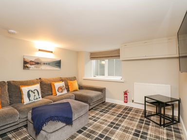 A living room with a brown sectional sofa with animal and orange pillows a plaid carpet and a black nesting table at Netherbeck Ambleside