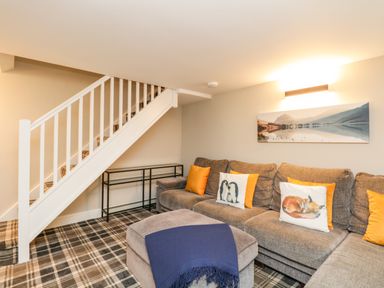 A living room with a sectional sofa and cushions under stairs with a plaid carpet at Netherbeck in Ambleside