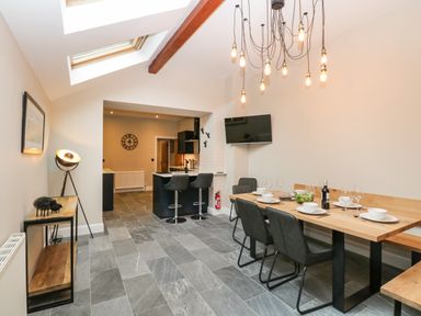 A dining area with table set for meals and chairs next to a kitchen area with bar stools under a skylight at Netherbeck in Ambleside