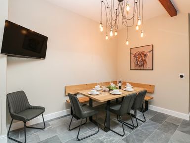 A dining area with a wooden table set with plates and glasses surrounded by black chairs and a wall-mounted TV in the corner at Netherbeck in Ambleside