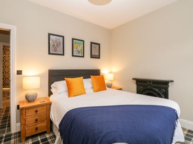 A bedroom with a double bed with orange pillows and navy throw a wooden nightstand with lamp and framed pictures on the wall Netherbeck Ambleside