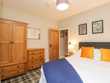 A bedroom with a bed with orange pillows a wooden wardrobe a wooden chest of drawers a bedside table with a lamp and framed pictures on the wall at Netherbeck in Ambleside