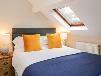 A bedroom with a double bed with yellow pillows blue blanket bedside tables and lamps under a skylight window at Netherbeck in Ambleside