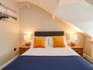 A bedroom with a bed with orange pillows a blue blanket and two bedside tables with lamps at Netherbeck in Ambleside