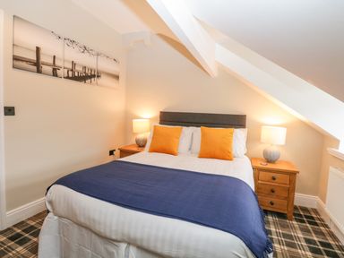 A bedroom with a double bed two orange pillows blue throw blankets two bedside tables each with a lamp and plaid carpet at Netherbeck in Ambleside