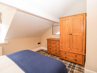 A bedroom with wooden wardrobe and chest of drawers next to a bed with blue blanket at Netherbeck in Ambleside