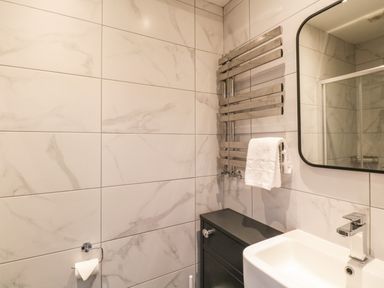 A bathroom with a sink a mirror a towel warmer with a white towel a cabinet and a toilet paper holder at Netherbeck Ambleside