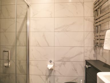 A bathroom with a glass shower door a toilet paper holder on tiled wall and a towel radiator at Netherbeck Ambleside