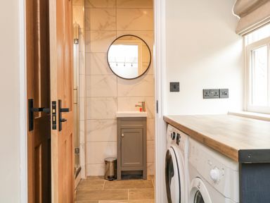 A utility room with a washing machine and dryer under a wooden countertop next to a bathroom with a sink and round mirror at Netherbeck in Ambleside