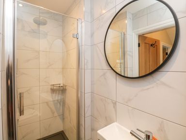 A bathroom with a glass shower enclosure a round mirror and a sink at Netherbeck Ambleside