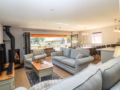 A living room with sofas a coffee table and a fireplace next to a dining area with a table set for guests at Lake View Lodge in Thorpe-On-The-Hill