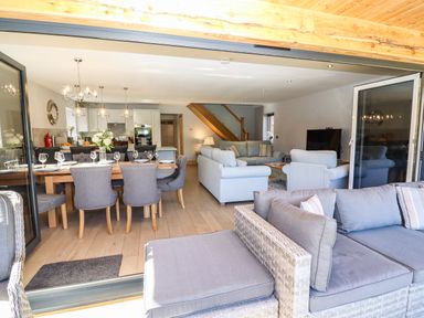 An open living and dining area with a dining table set with glasses and plates a kitchen with pendant lights two sofas and a television at Lake View Lodge in Thorpe-On-The-Hill