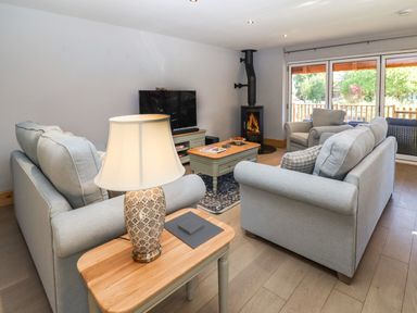 A living room with sofas a wood burning stove a TV and large windows at Lake View Lodge in Thorpe-On-The-Hill