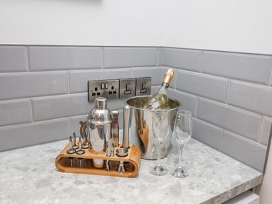 A kitchen counter with a cocktail shaker set bottle in an ice bucket and two wine glasses at Lake View Lodge in Thorpe-On-The-Hill