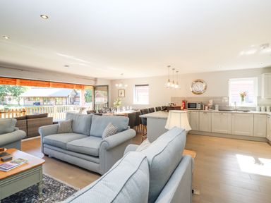 An open living room and kitchen with sofas, dining table, kitchen island, and large windows at Lake View Lodge in Thorpe-On-The-Hill