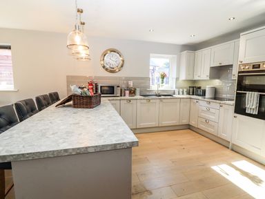 A kitchen with an island counter with chairs a wall clock and cabinets at Lake View Lodge in Thorpe-On-The-Hill