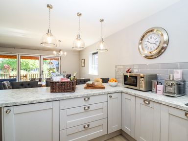 A kitchen with a marble countertop microwave a clock on the wall and a basket of food at Lake View Lodge in Thorpe-On-The-Hill