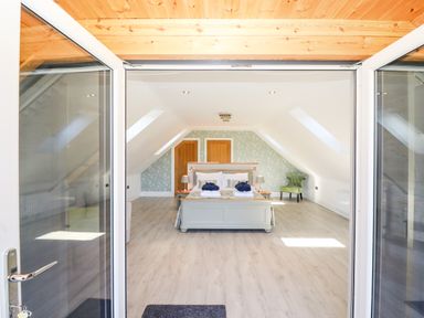A bedroom with a double bed two wooden doors and a green armchair at Lake View Lodge in Thorpe-On-The-Hill