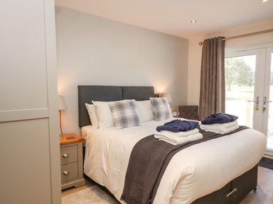 A bedroom with a double bed with pillows and folded clothes on it bedside tables with lamps and a window with curtains at Lake View Lodge in Thorpe-On-The-Hill
