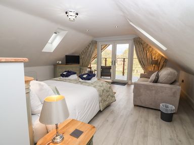 A bedroom with a bed sofa bedside table and lamp TV unit and glass doors leading to a balcony at Lake View Lodge in Thorpe-On-The-Hill