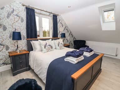 A bedroom with a double bed navy blue bedding and peacock wallpaper at Lake View Lodge in Thorpe-On-The-Hill