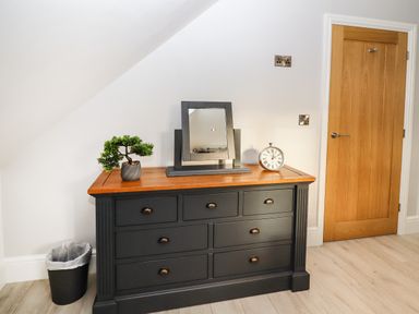 A black dresser with a wooden top holding a small plant a mirror and a clock next to a wooden door at Lake View Lodge in Thorpe-On-The-Hill