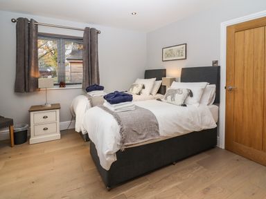 A bedroom with two single beds bedside tables lamps a window with curtains and a wooden door at Lake View Lodge in Thorpe-On-The-Hill