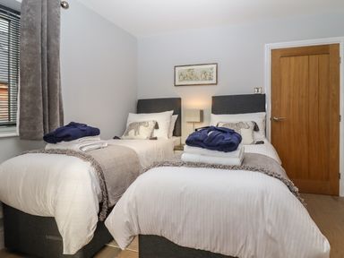 A bedroom with two single beds with gray headboards white bedding and folded towels and robes on top at Lake View Lodge in Thorpe-On-The-Hill